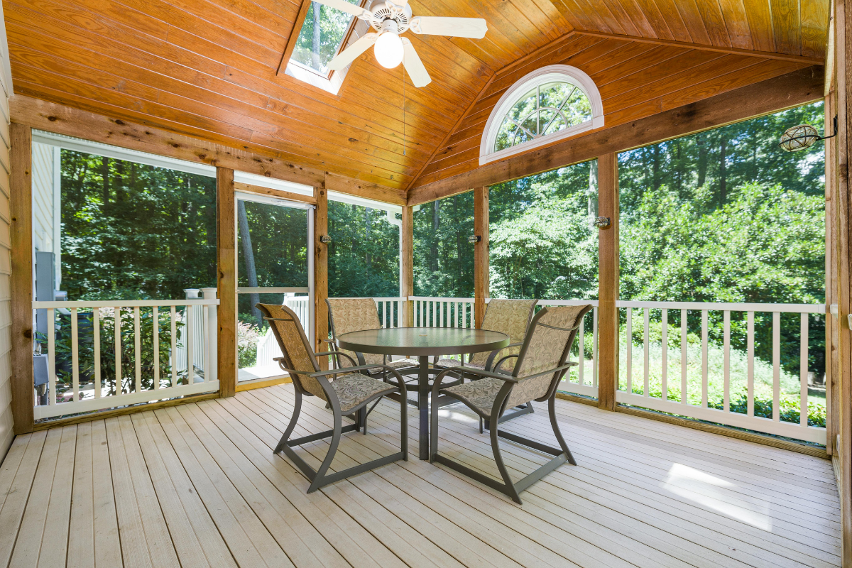 Screened in porch addition cost example showing a newly built residential screened porch with ceiling fan outdoor furniture and fiberglass screens